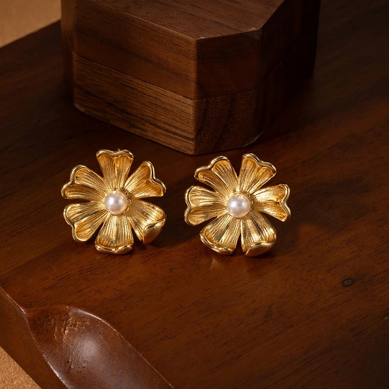 Gold flower-shaped earrings with pearl centers on a wooden surface
