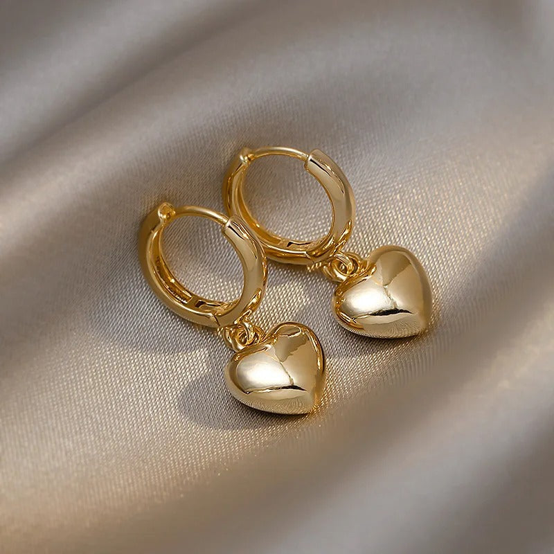 Shiny gold hoop earrings with heart pendants, romantic and minimalist jewellery design placed on smooth silk fabric