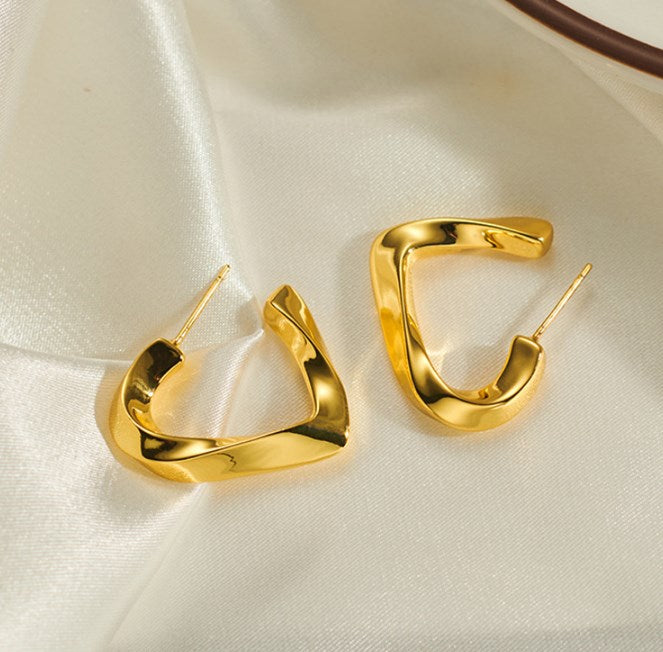 Shiny gold heart-shaped earrings placed on satin fabric, trendy lightweight jewelry for women’s daily and party wear.