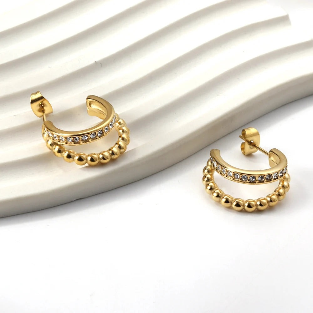 A pair of gold-colored, double-layered, diamond-studded earrings with a cc shape, displayed on a white surface.