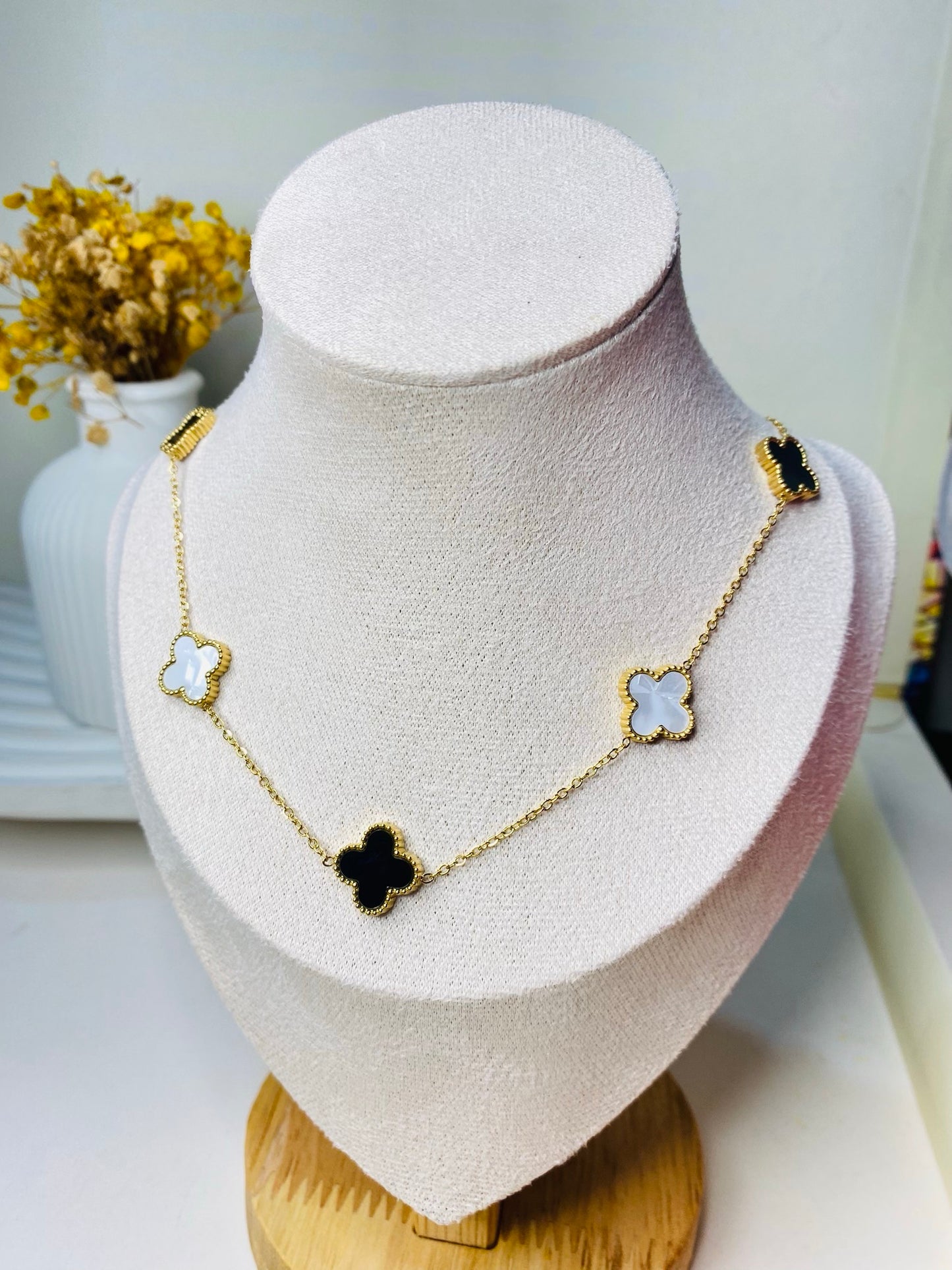 A gold-plated chain necklace featuring black and white clover-shaped pendants displayed on a white mannequin bust.