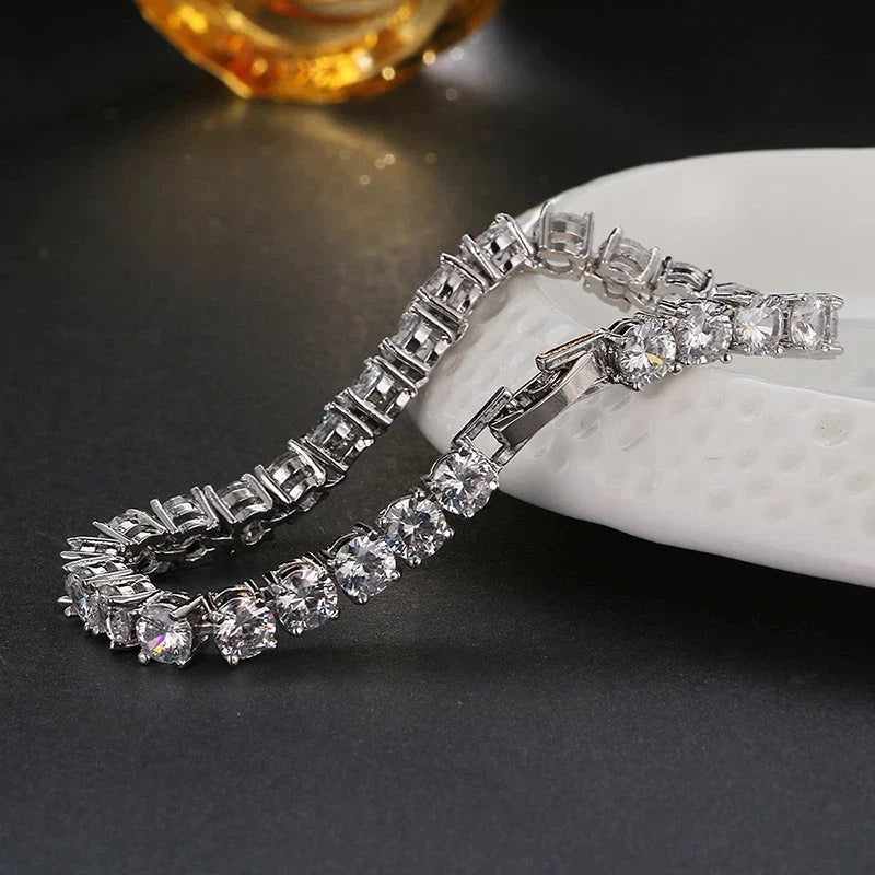 Elegant silver tennis bracelet with shiny square-cut stones placed on a white ceramic surface.