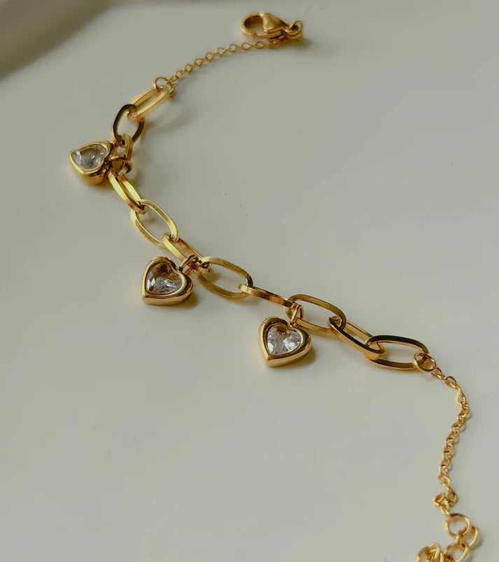 Gold chain link bracelet with three heart-shaped pendants and white stones.