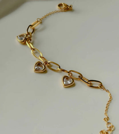 Gold chain link bracelet with three heart-shaped pendants and white stones.