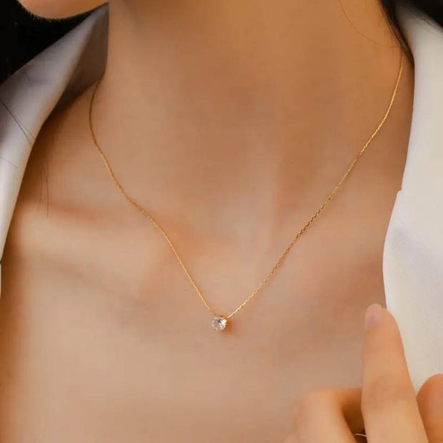 Minimalist gold necklace with single round diamond pendant worn by woman.