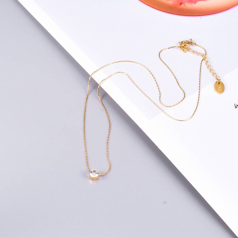 Delicate gold chain necklace with solitaire diamond pendant placed on magazine background.