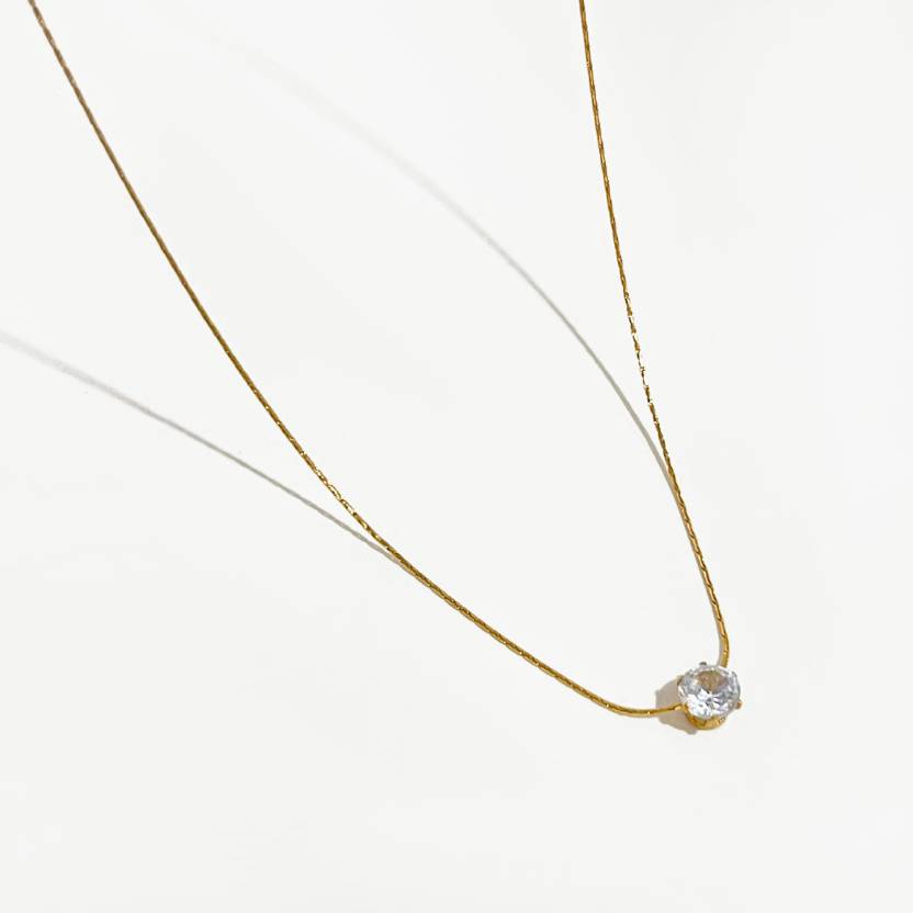 Minimalist gold chain necklace with single solitaire diamond pendant on white background.