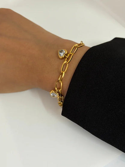 Model wearing a gold chain link bracelet with heart-shaped white stone charms.
