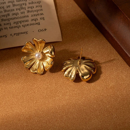 Gold flower-shaped earrings on a textured surface with a book in the background