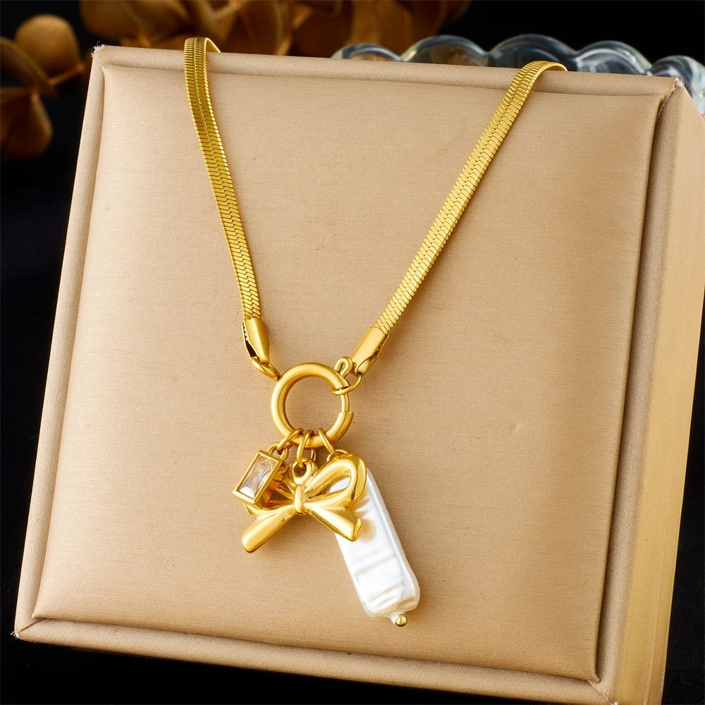 Gold necklace with a bow and pearl charm on a beige box