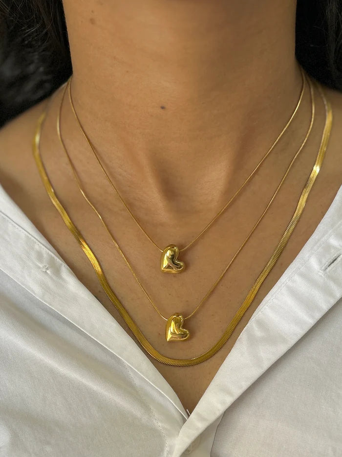Layered gold necklaces with dainty heart pendants and sleek flat chain, elegant jewelry styling for women.