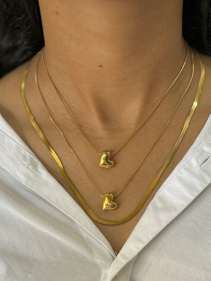 Layered gold necklaces with dainty heart pendants and sleek flat chain, elegant jewelry styling for women.
