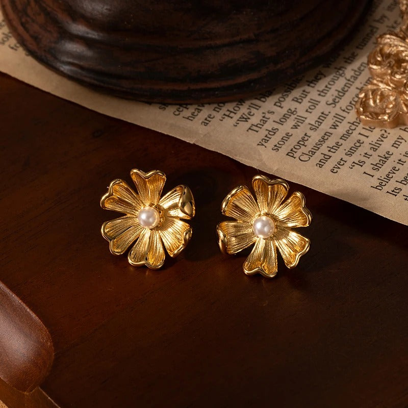 Gold flower-shaped earrings with pearl centers on a wooden surface.