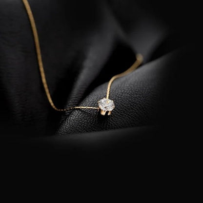 Minimalist gold chain necklace with solitaire diamond pendant placed on black fabric background.