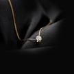 Minimalist gold chain necklace with solitaire diamond pendant placed on black fabric background.