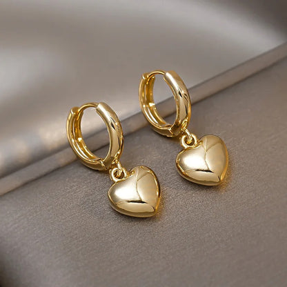 Elegant gold hoop earrings with dangling puffed heart charms, luxury fashion jewellery displayed on grey satin surface