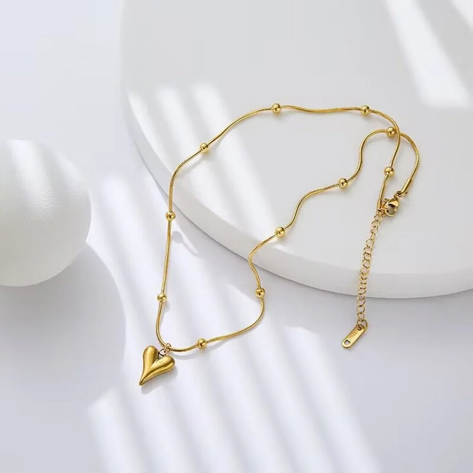 Stylish gold beaded chain necklace with heart pendant displayed on minimal white background.