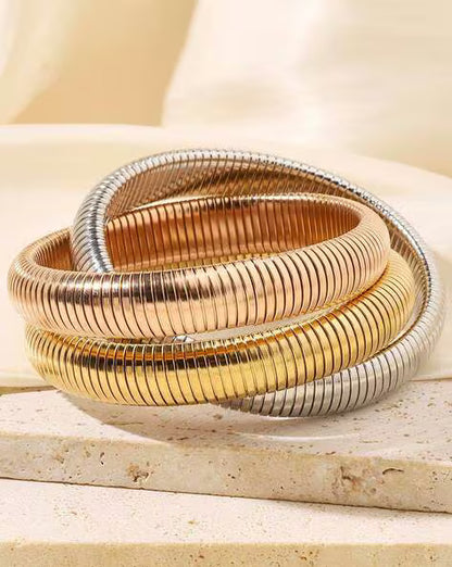 A set of three interlocking snake coil bangle bracelets in gold, rose gold, and silver colors.