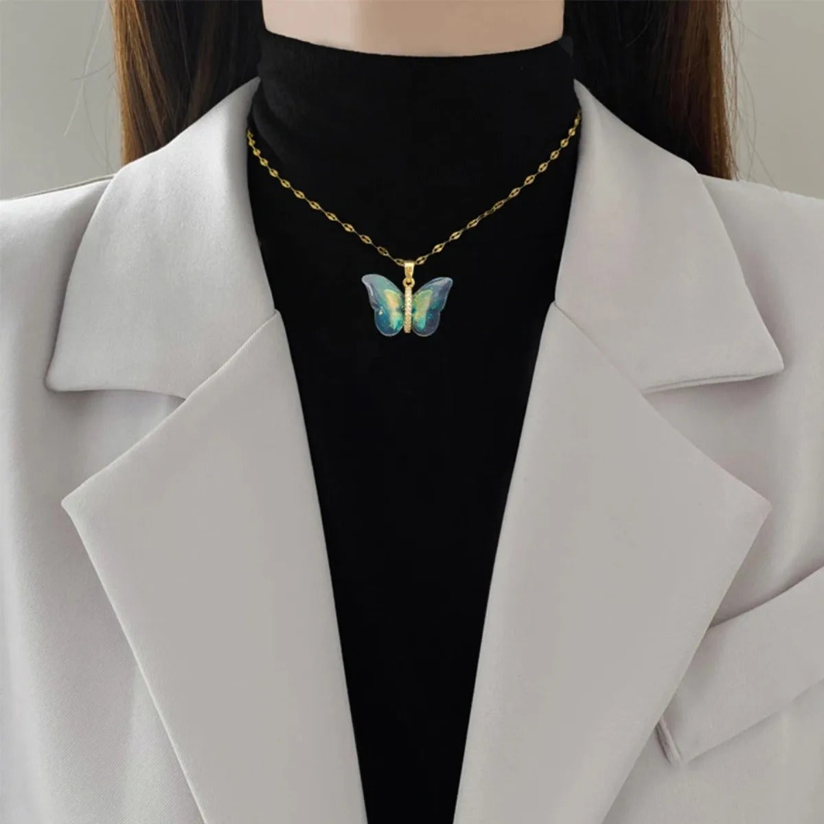 Person wearing a gold necklace with a butterfly pendant on a plain background