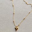 Elegant gold necklace with a central heart pendant and delicate bead accents on fine chain, displayed on soft beige background.