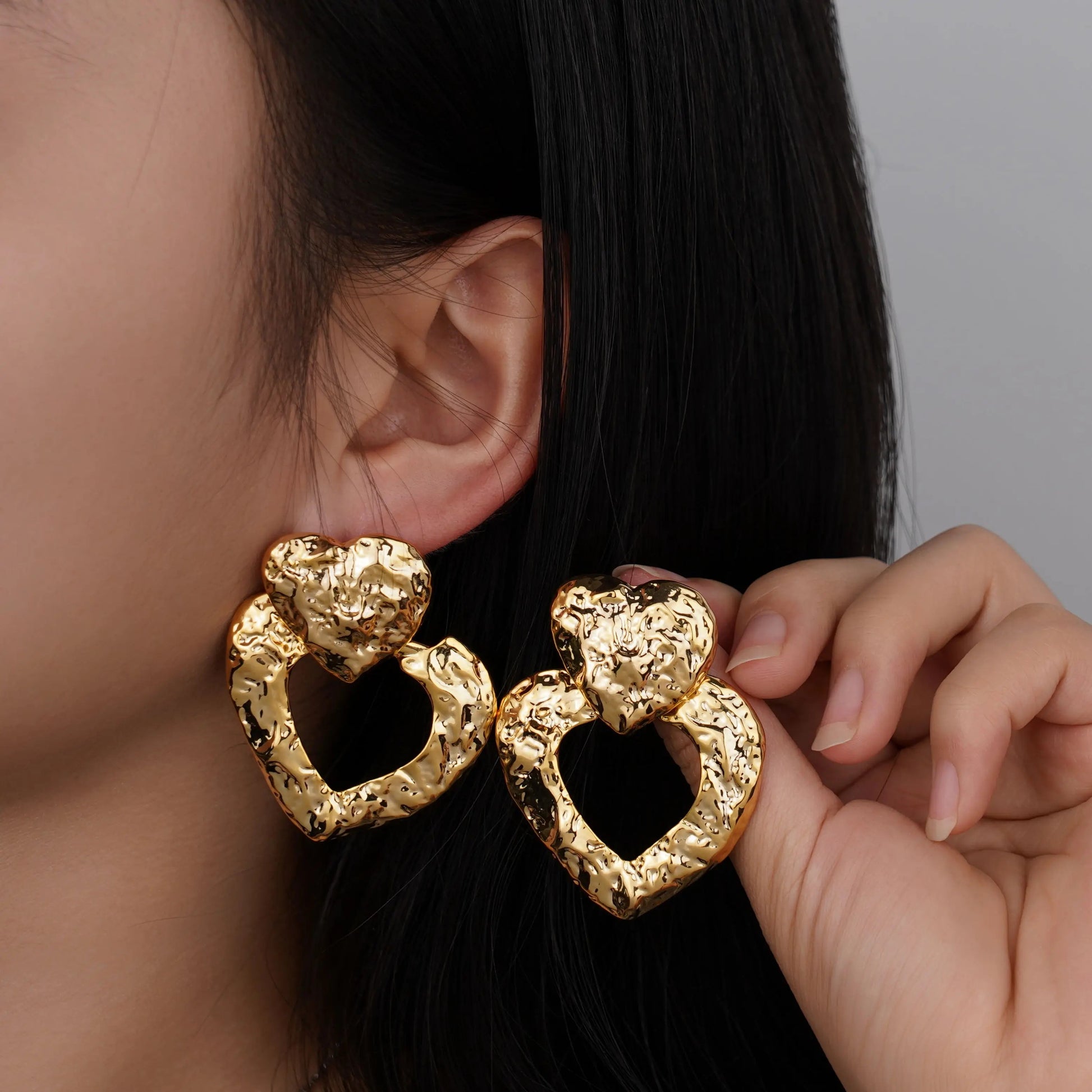 Gold heart-shaped earrings worn by a person with a neutral background