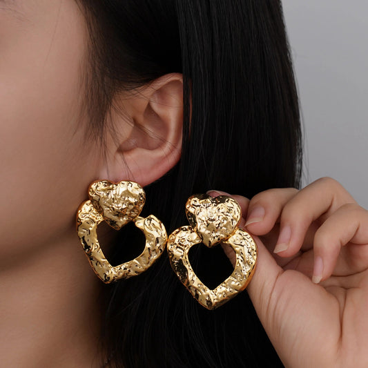 Gold heart-shaped earrings worn by a person with a neutral background