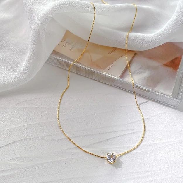 Elegant gold chain necklace with solitaire diamond pendant placed on white fabric background.