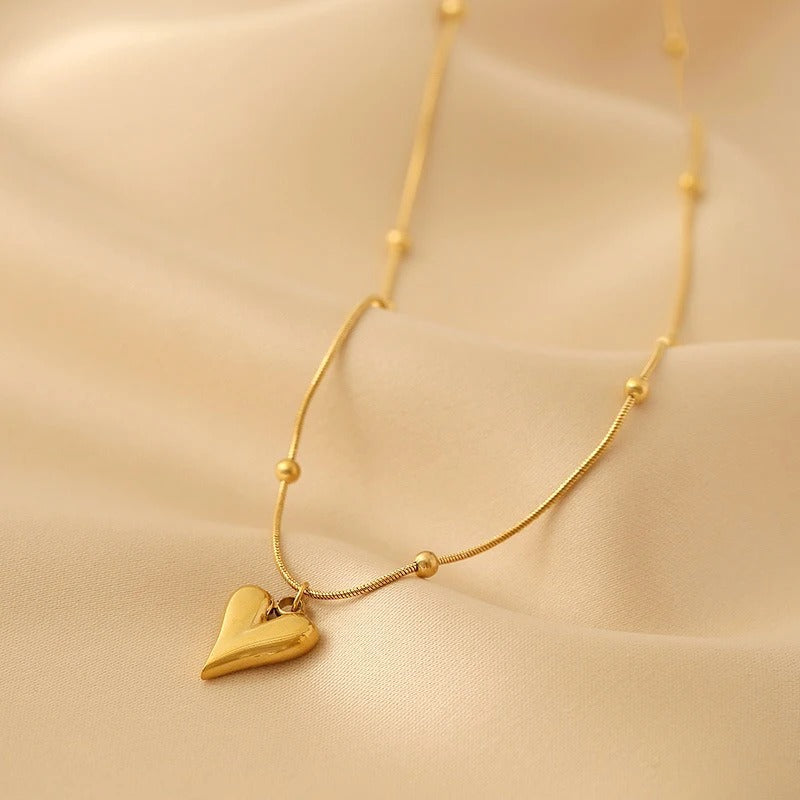 Elegant gold heart pendant necklace with delicate beaded chain on golden satin fabric.