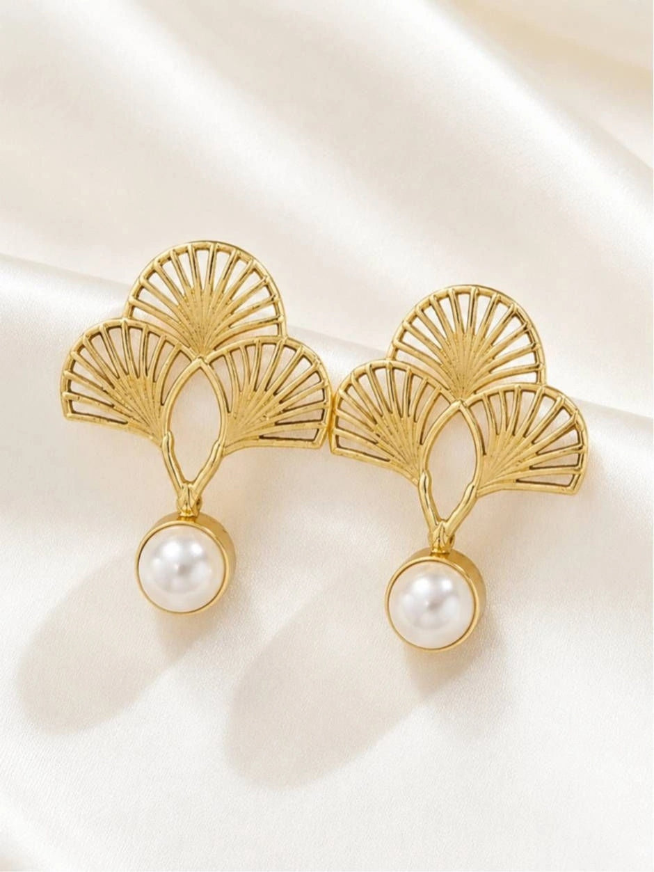 Close-up of two gold openwork fan earrings with pearl drops on white fabric
