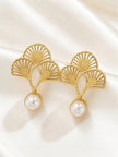 Close-up of two gold openwork fan earrings with pearl drops on white fabric