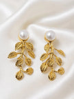 Pair of gold-plated leaf drop earrings with faux pearl studs laid flat on white satin