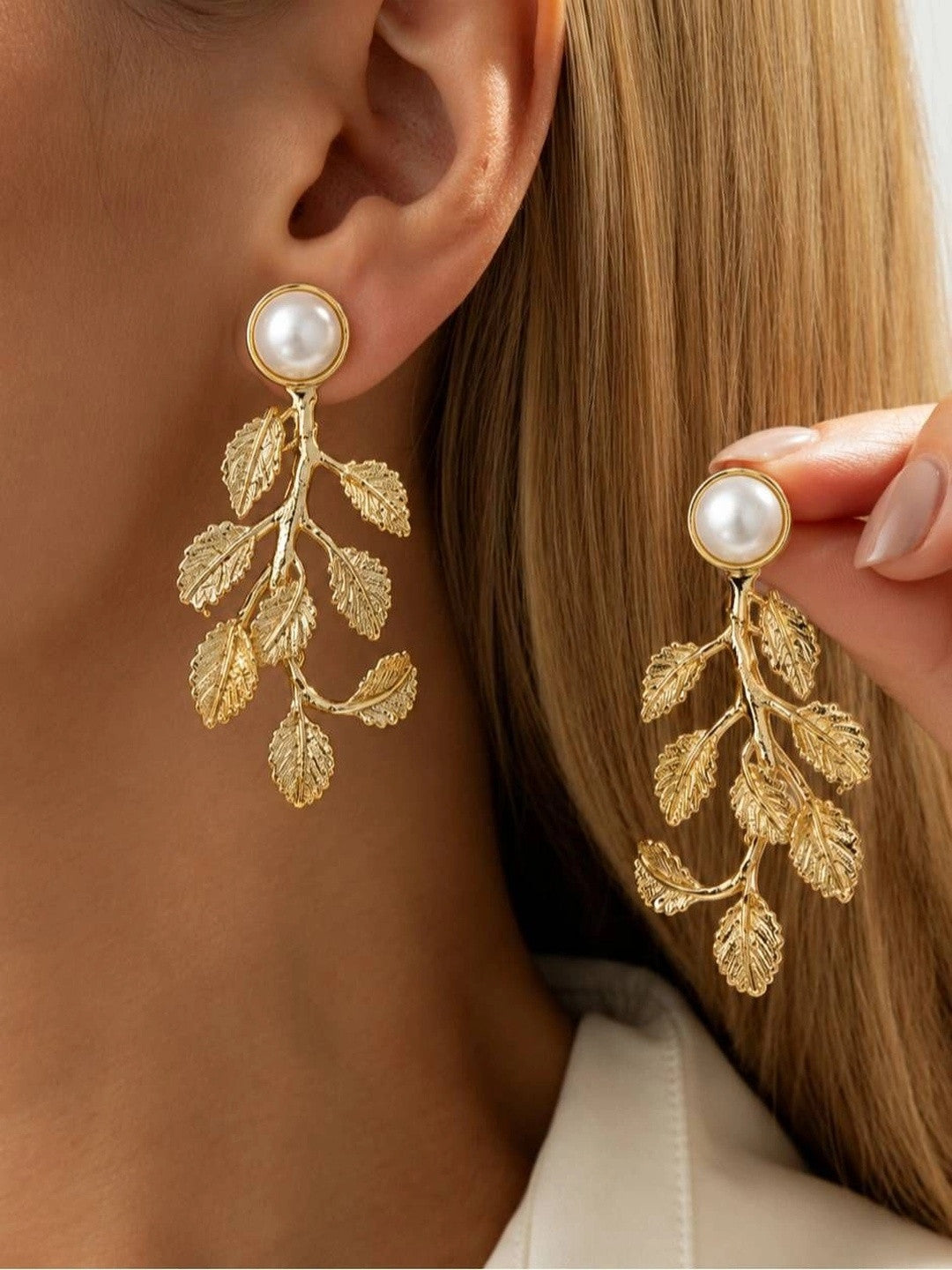 Model wearing gold pearl leaf drop earrings, one ear shown and one held up to show scale