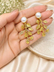 Close-up of gold leaf drop earrings with pearl tops resting on a model's open palm