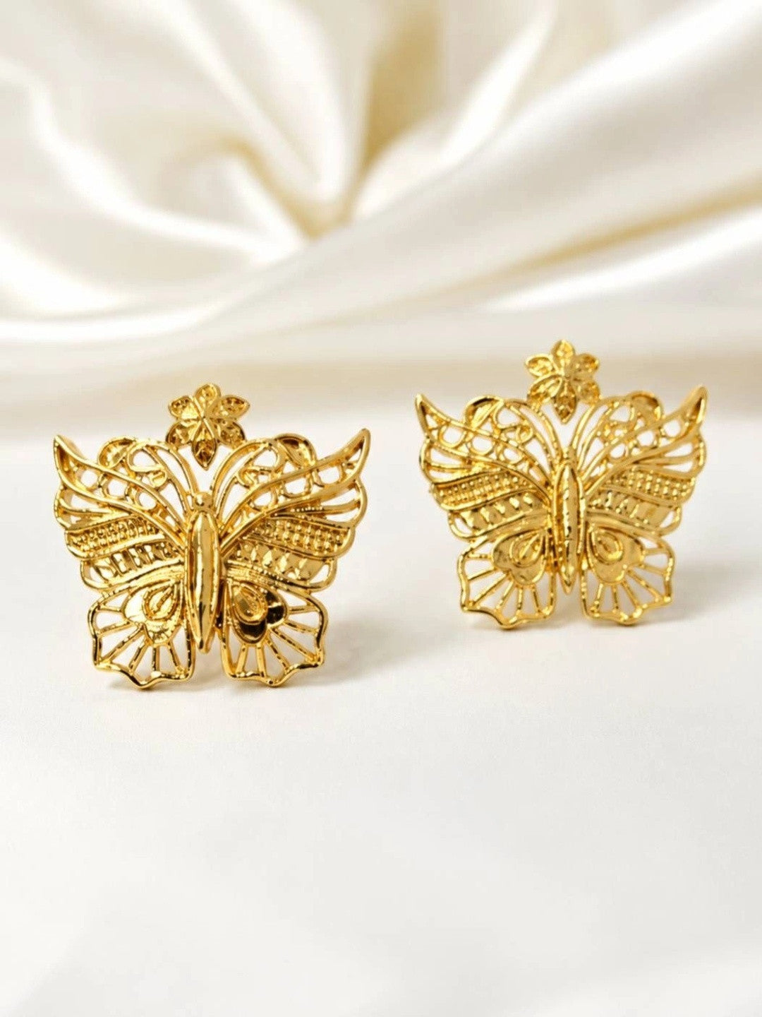 Pair of gold-plated filigree butterfly stud earrings displayed upright on white satin