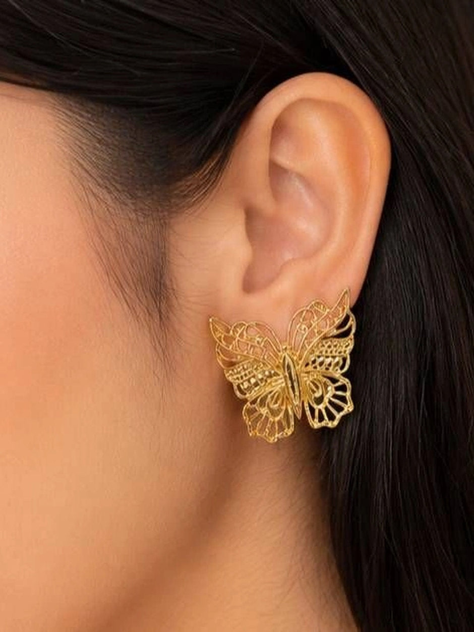 Gold butterfly stud earring worn on a woman's ear showing scale and fit