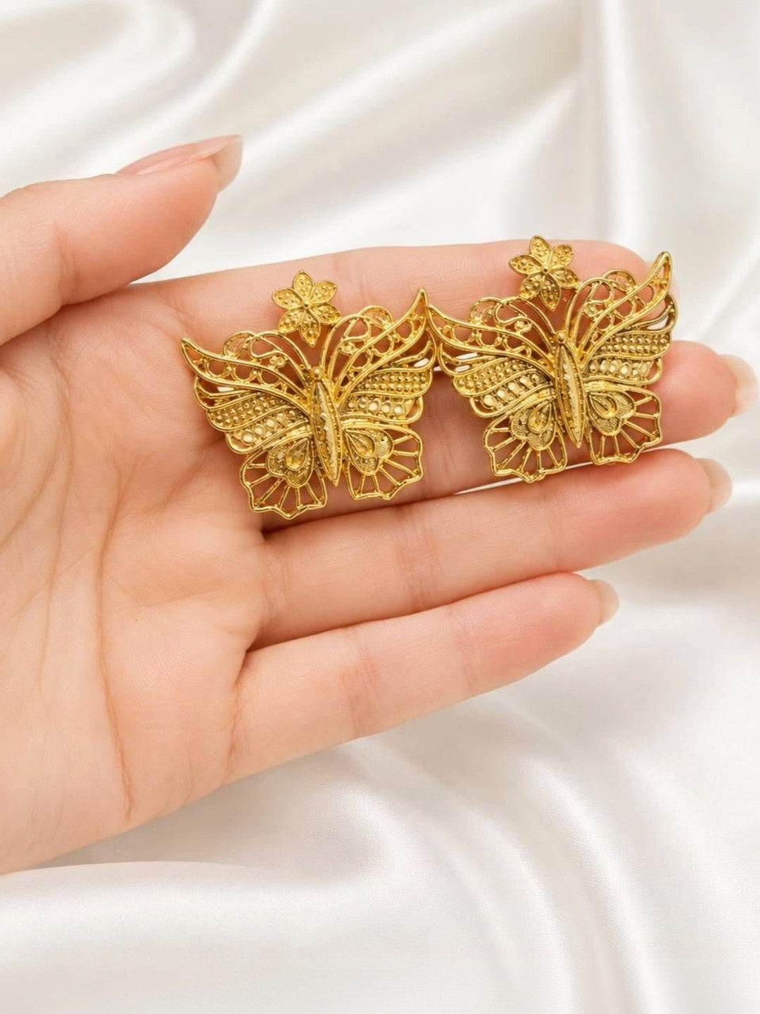Two gold filigree butterfly stud earrings resting on an open palm for size reference