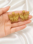 Two gold filigree butterfly stud earrings resting on an open palm for size reference