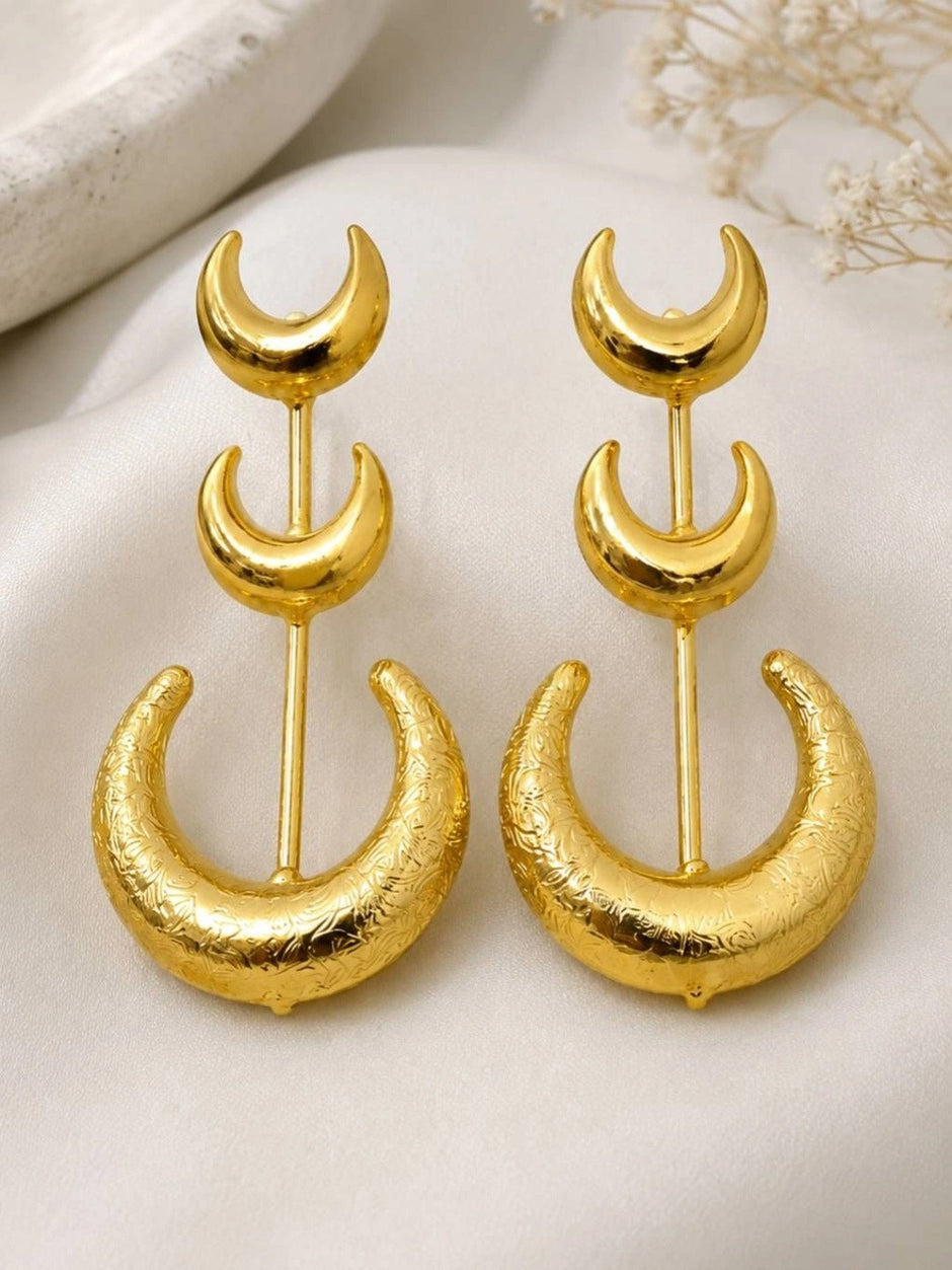 Front view of gold-plated triple crescent moon drop earrings laid flat on white satin fabric