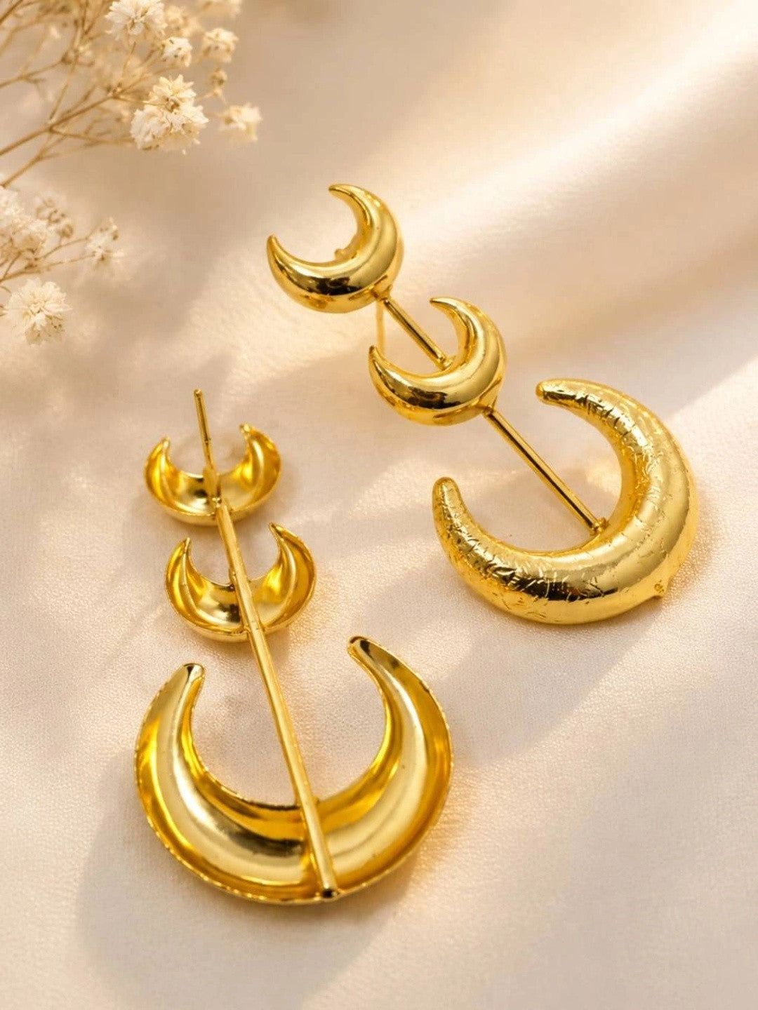 Back view of gold-plated crescent moon earrings showing stud post mechanism on satin surface