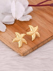 Two gold starfish stud earrings displayed side by side on a wooden surface showing textured arm detail
