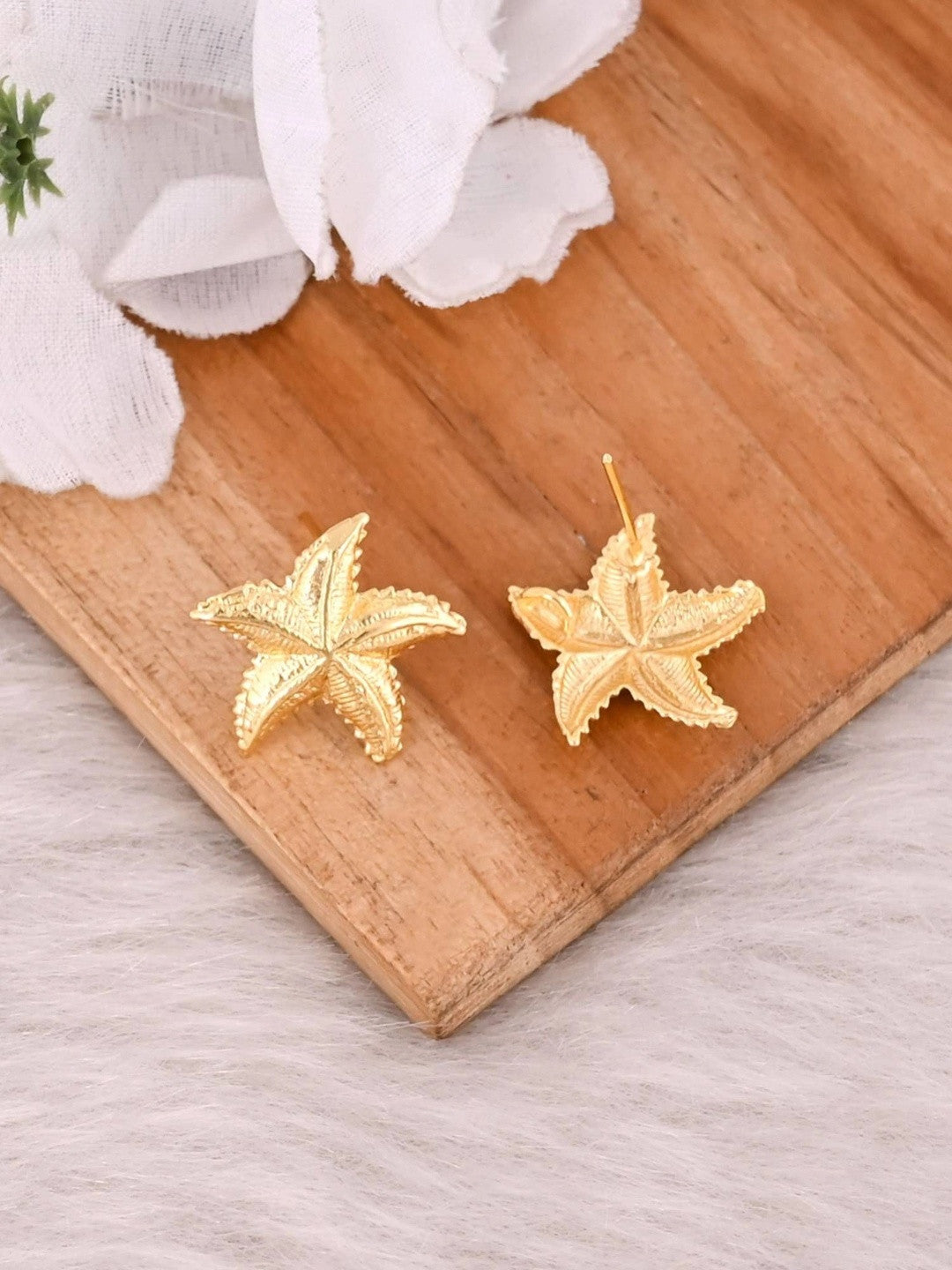 Gold starfish stud earrings on wooden board, one showing the front face and one showing the reverse with post fitting