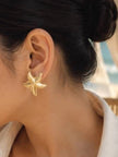 Woman with dark hair in a bun wearing a gold starfish stud earring, seen from behind against a soft outdoor backdrop