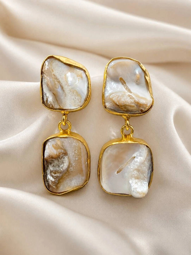 Pair of gold-plated baroque pearl drop earrings laid flat on ivory satin fabric