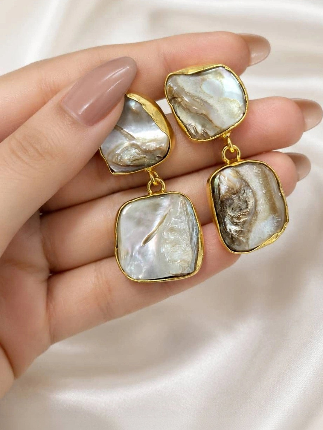 Hand holding pair of gold-plated baroque pearl drop earrings showing size and natural pearl variation