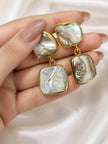 Hand holding pair of gold-plated baroque pearl drop earrings showing size and natural pearl variation