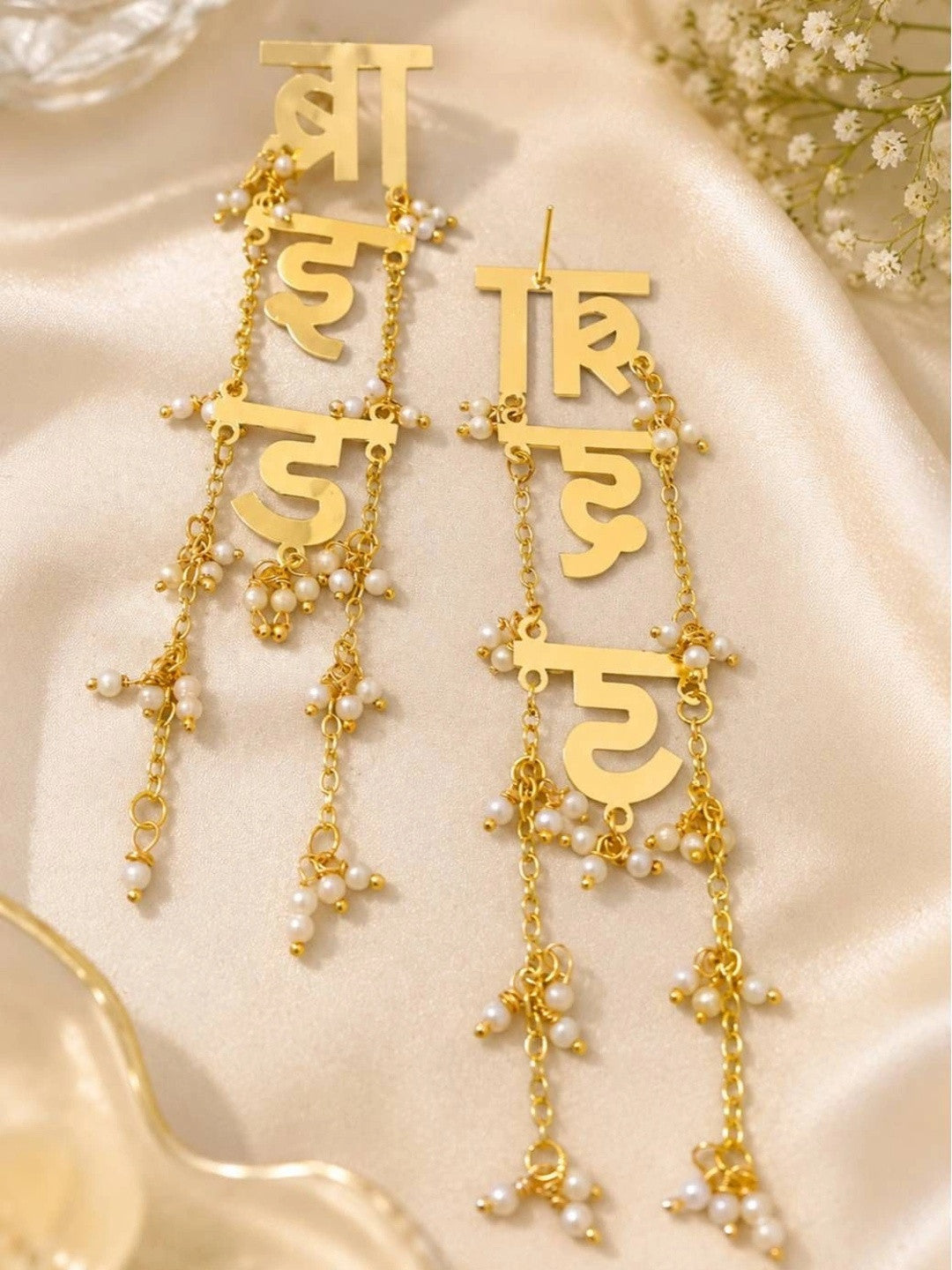 Both gold Hindi script bride earrings laid flat on cream satin fabric showing Devanagari lettering and pearl clusters