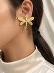 Gold dragonfly stud earring worn on a woman's ear against a white satin background