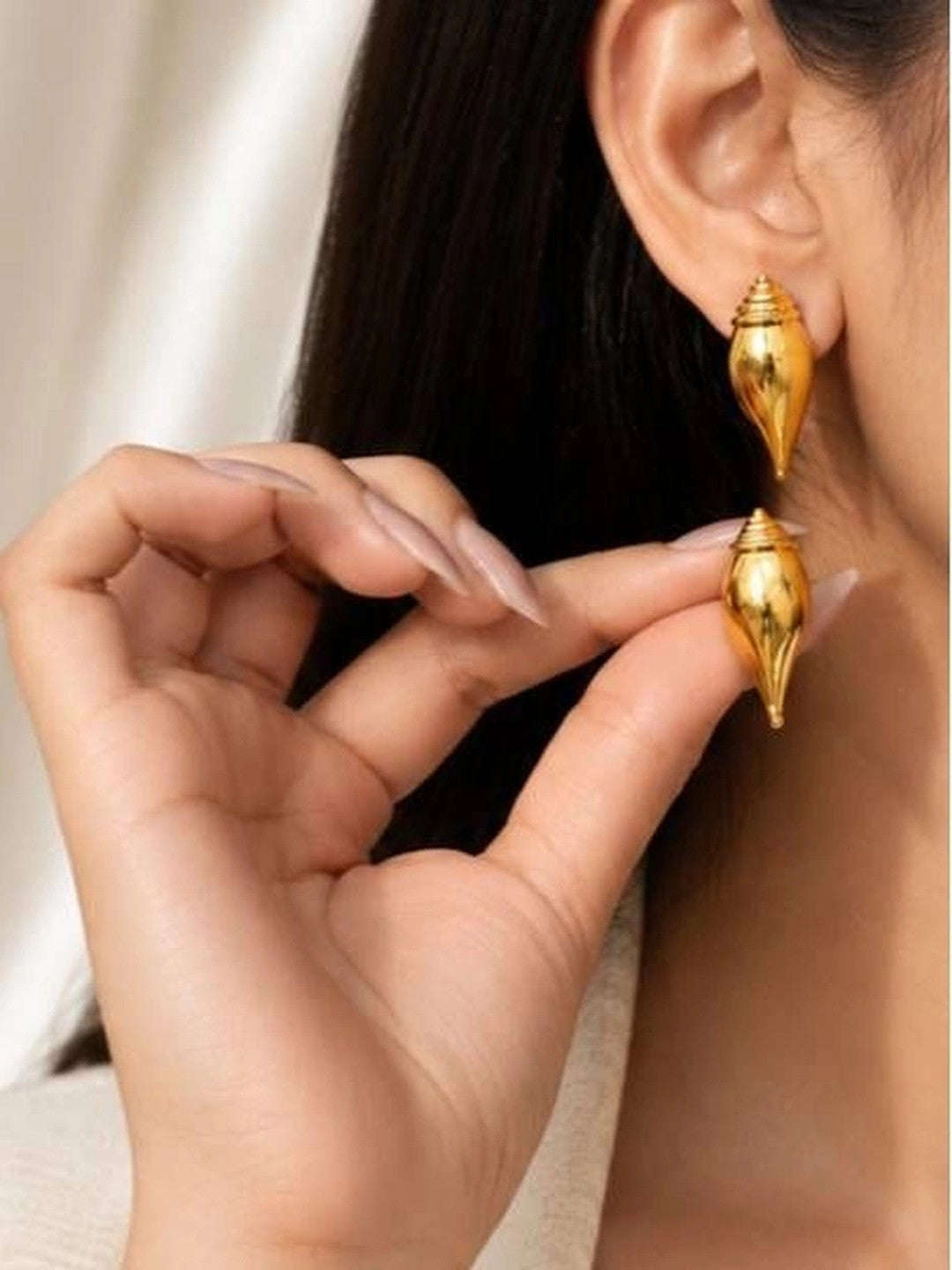 Woman wearing gold conch shell stud earrings, shown from side profile close to ear