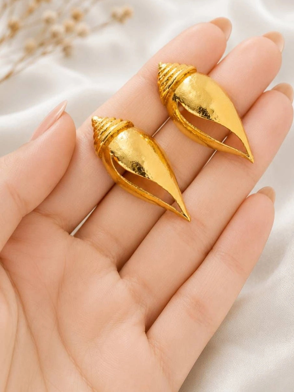 Two gold-plated conch shell earrings resting in an open palm showing scale and texture