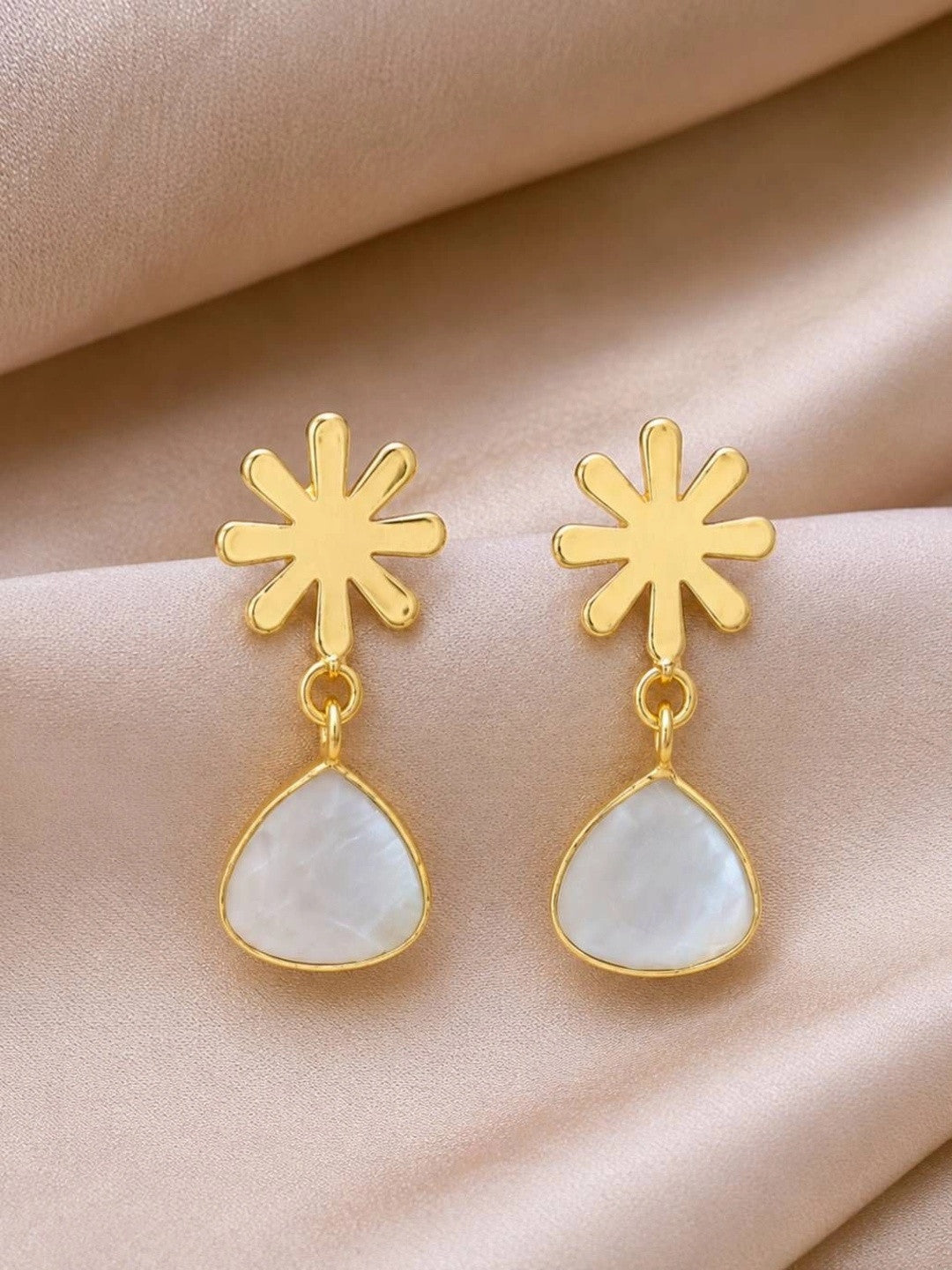 Pair of gold-plated snowflake stud drop earrings with milky white teardrop pendants on a peach satin background